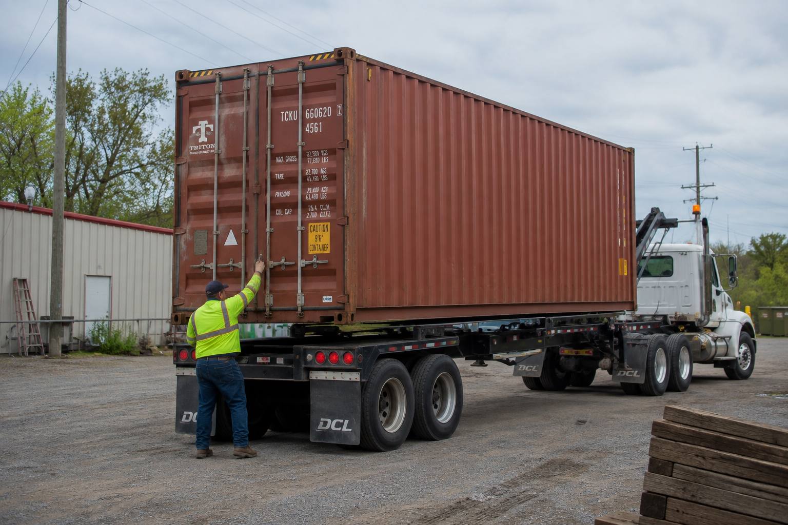 Used 40ft container loaded and strapped on a tilt-bed trailer, checked by the driver before it leaves the yard